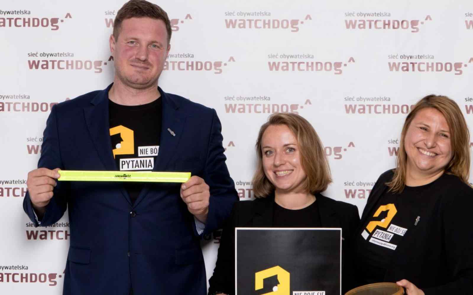 Zdjęcie Kasi Batko-Tołuć i dwóch innych osób na tle ścianki zdjęciowej z logo "sieć obywatelska - watchdog"