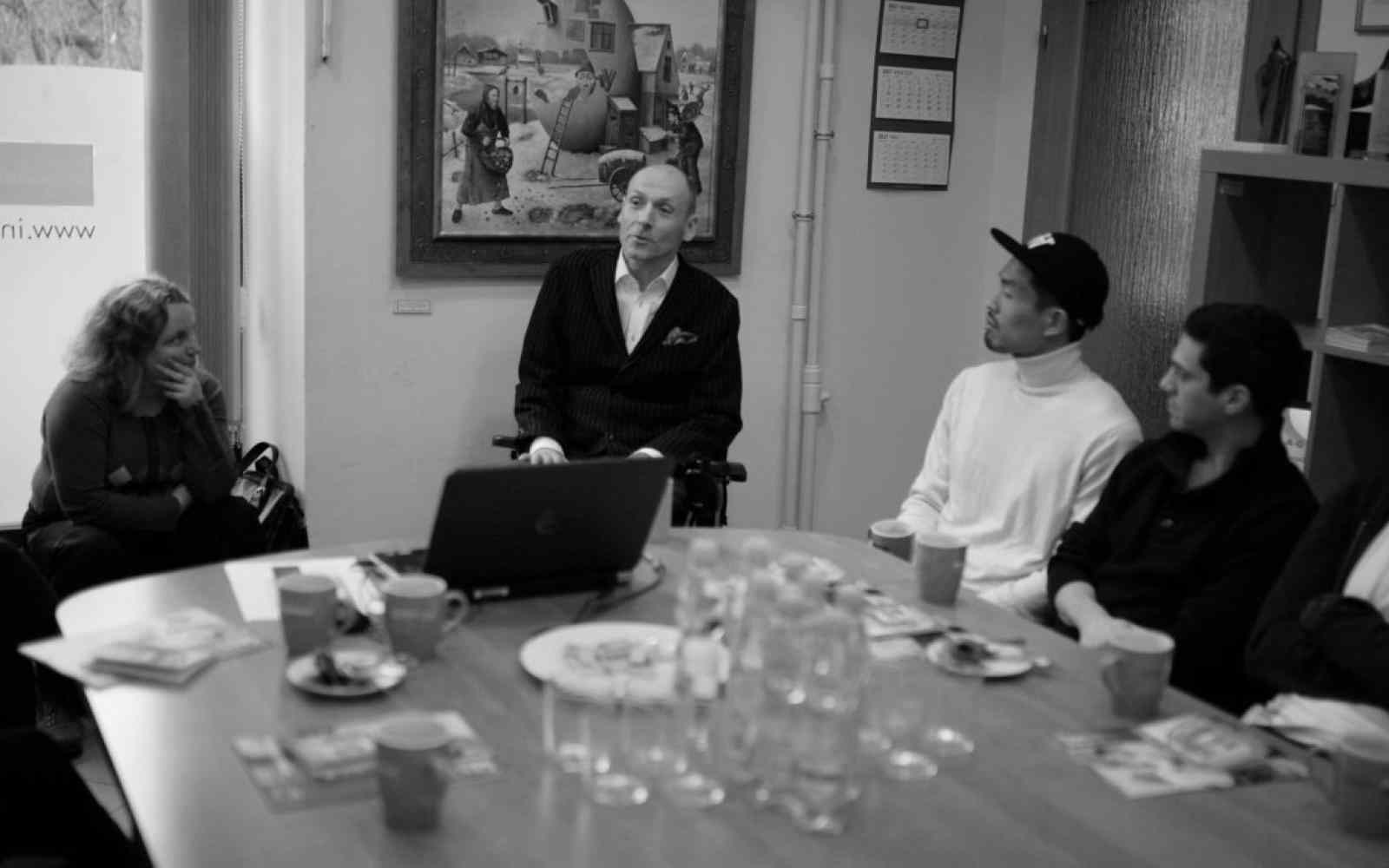 Czarno-białe zdjęcie Piotra Pawłowskiego - mówi do osób siedzących przy dużym stole.
