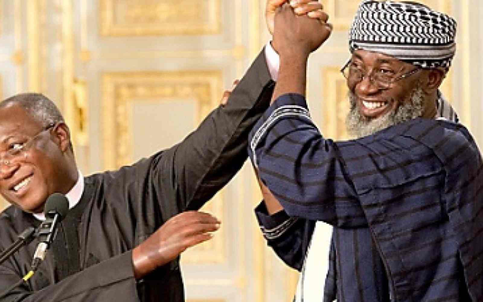 Wspólne zdjęcie pastora Jamesa Wuye i imama Mohammeda Ashafy. Ich złączone ręce są uniesione do góry, obaj się uśmiechają.