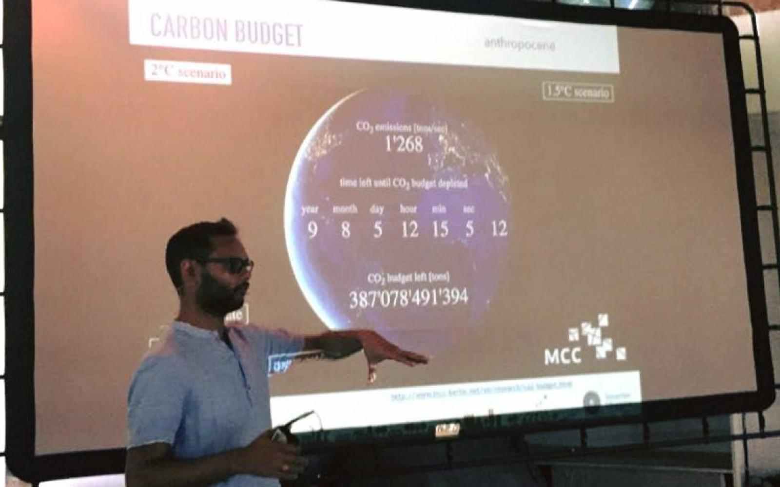 Zdjęcie przedstawia Srirama Kuchimanchi wygłaszającego prezentację. Na slajdzie za nim znajdują się dane dotyczące emisji CO2.