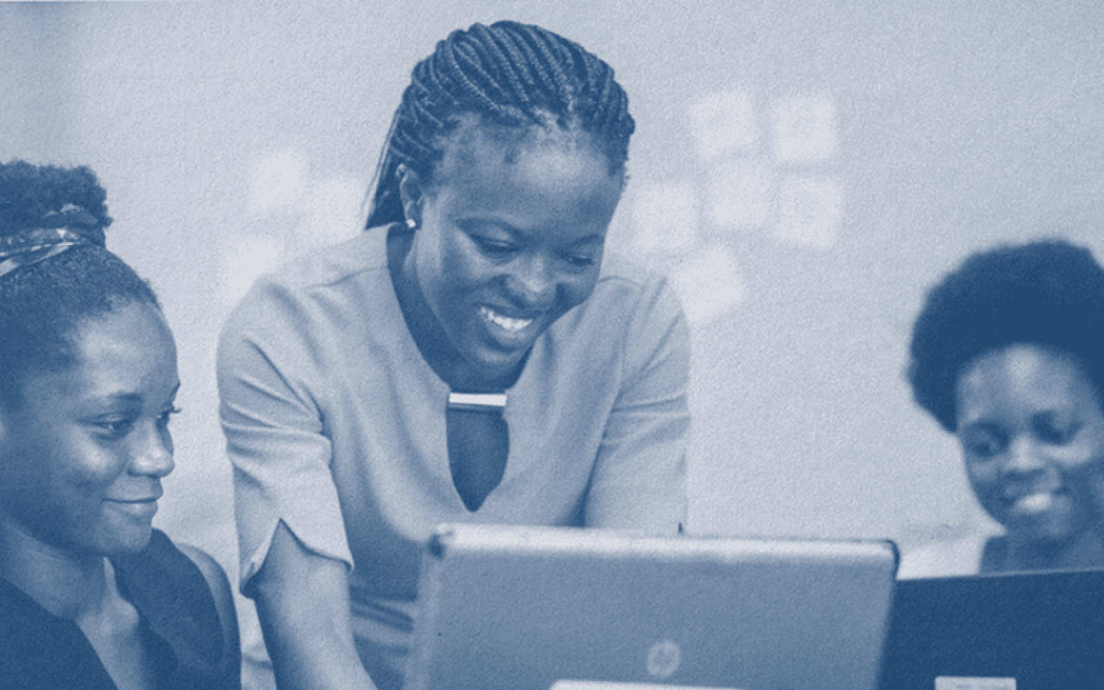 Photo shaded in dark blue. Three people huddle over a few laptops, smiling and looking at the laptops, as if they are working on something together