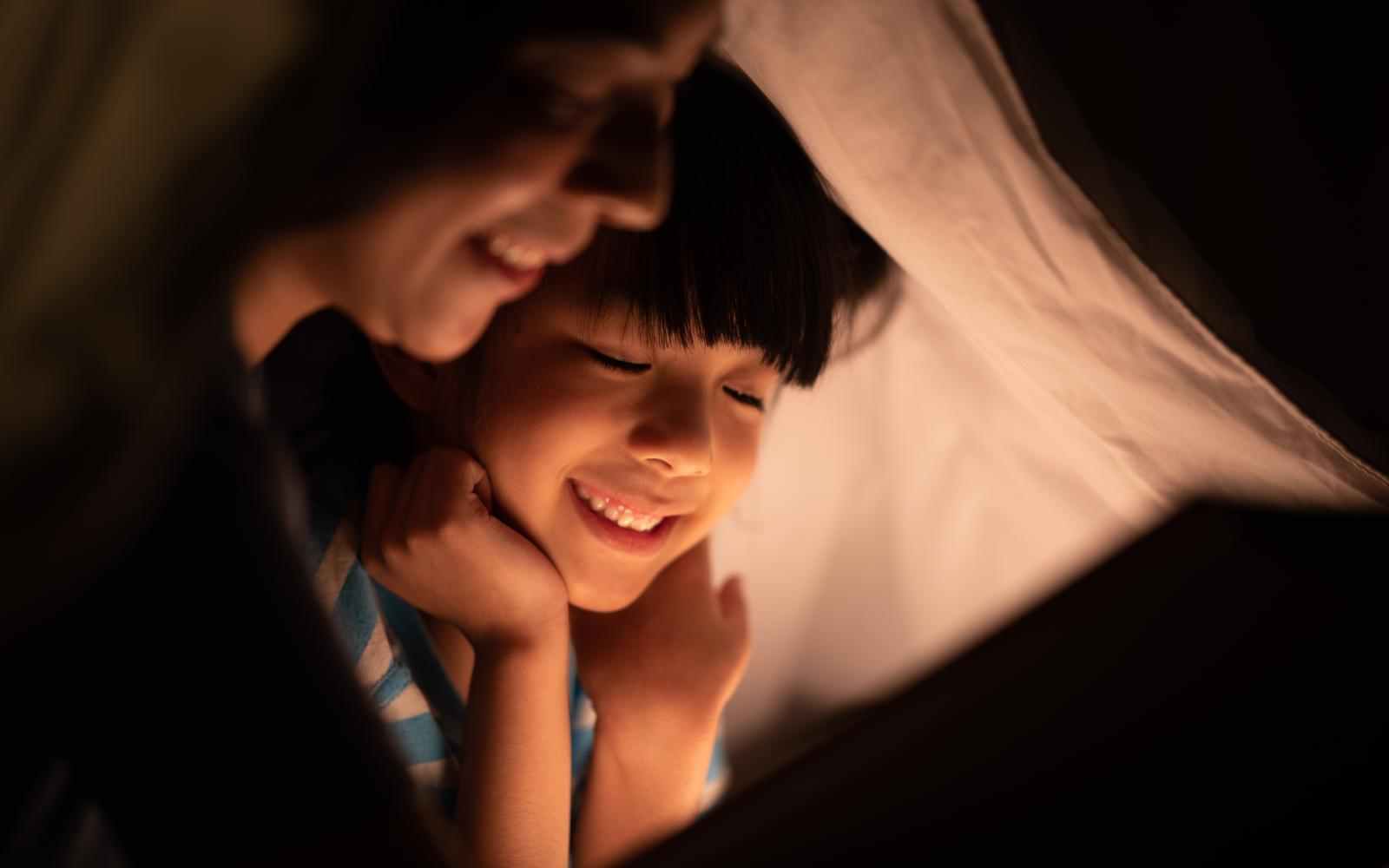 young Asian mother read the story in the book for her daughter children on the bed at home, family and motherhood learning concept