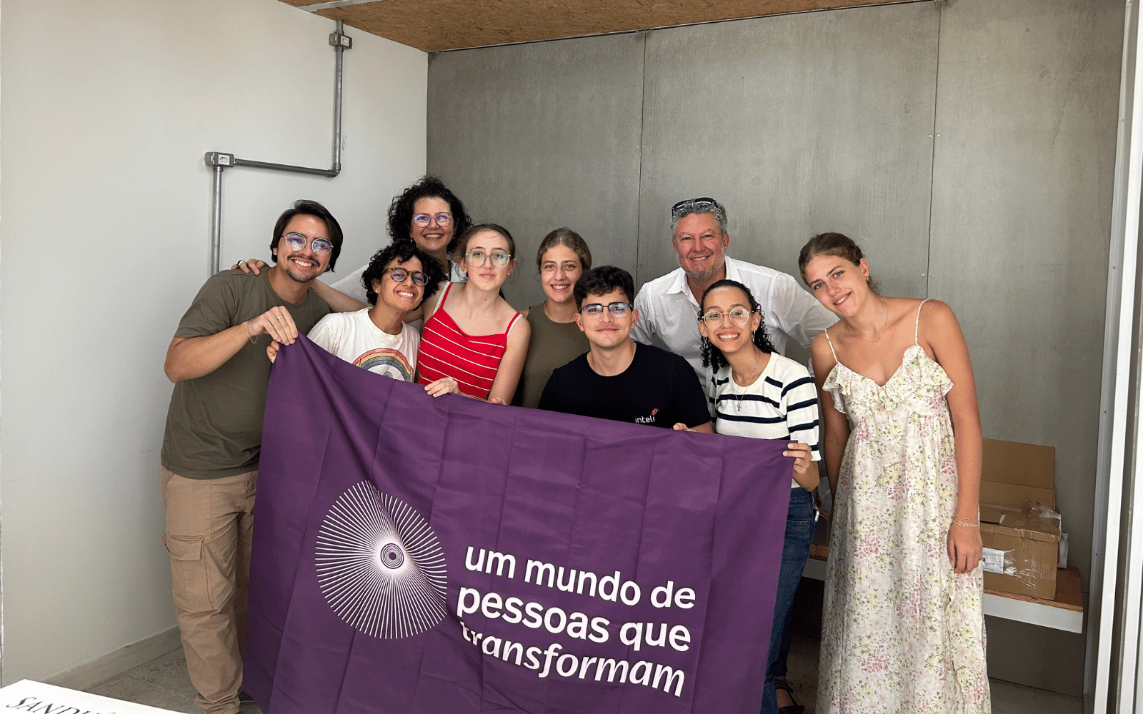 Vê-se uma foto da equipe Ashoka, juntamente com os Jovens Transformadores e Alejandro Villanueva e suas filhas. Na fotografia todos estão segurando a bandeira do movimento Um Mundo de Pessoas que Transformam