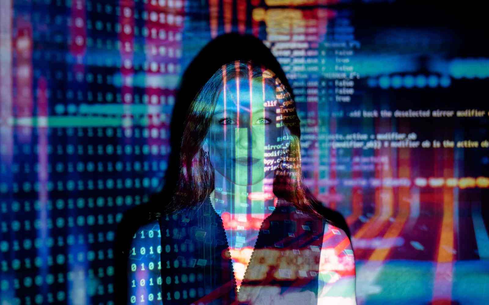 Mujer mirando a cámara en la que se reflejan códigos de programación 