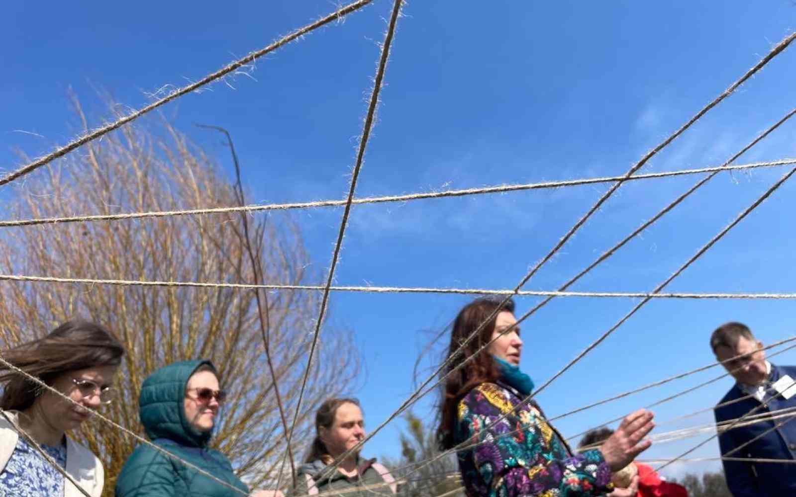 73 / 5 000 A group of people standing outside holding strings that connect them like a net.