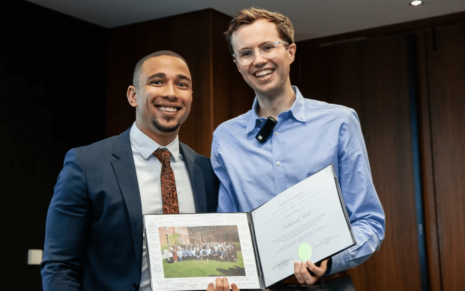 Ashoka Fellow Scott Stirrett (right, lighter skin glasses and shorter brown hair) with Nathaniel Scott (left, brown skin, dark short hair in a fade, goatee). Both people dressed in formal wear smiling at the camera. Background 
