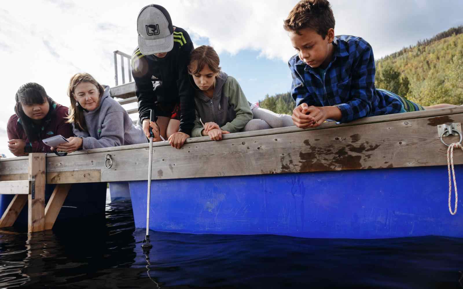 Group of youth as well as some parents monitoring water data off the side of a dock