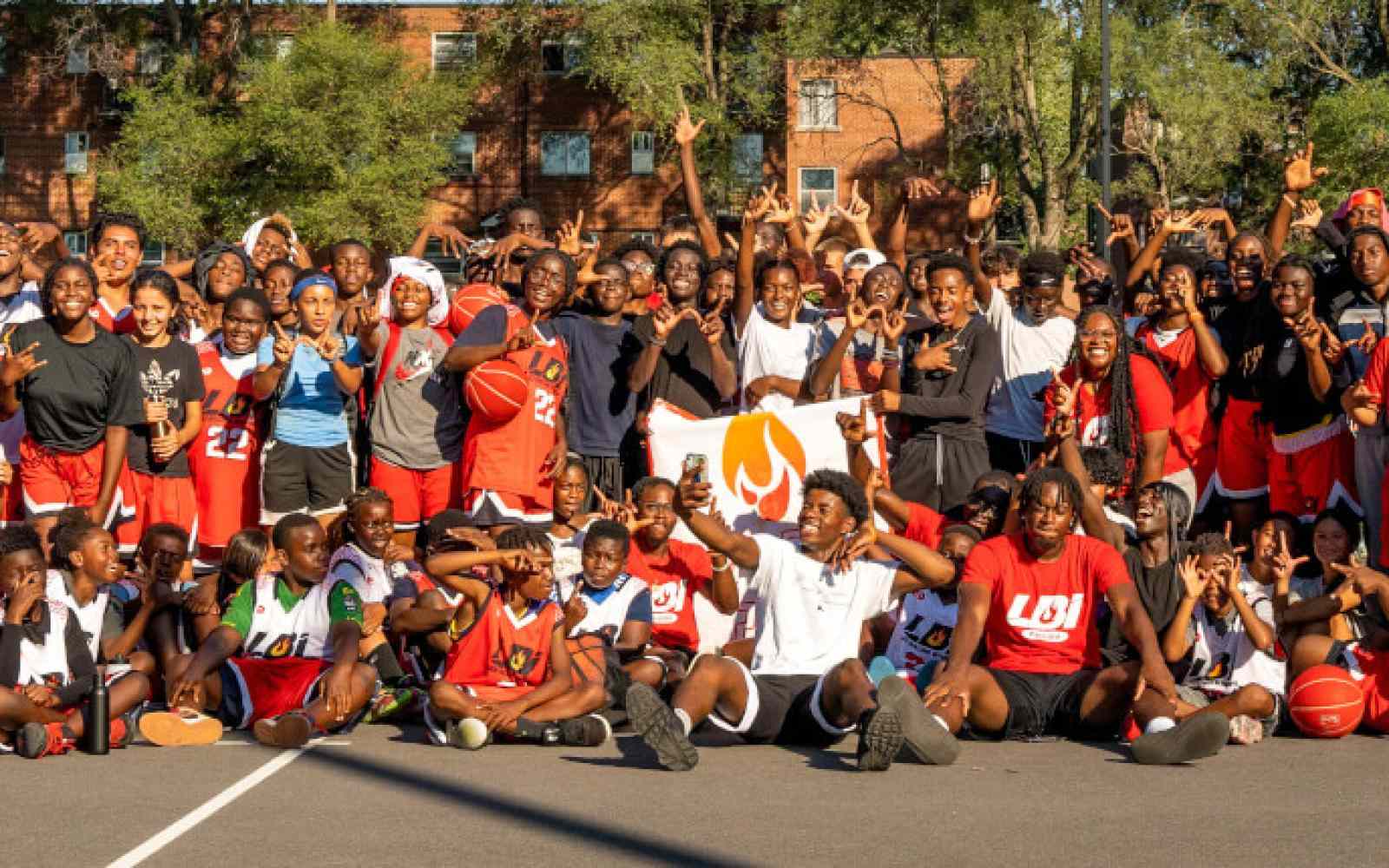 Banner of youth participants involved with Les Ballons Intensifs; about 100 youth of diverse backgrounds lined up in three rows on a basketball court smiling at the camera