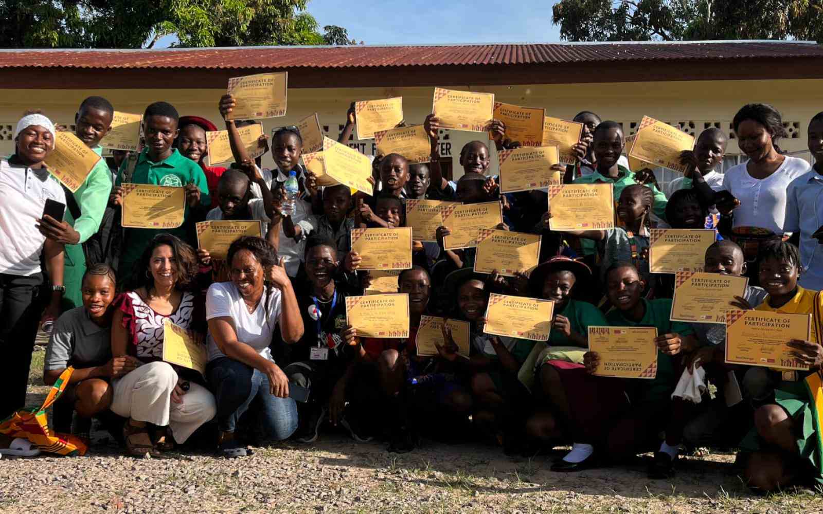 Group of young people and community members in Sierra Leone holding signs and smiling at the camera (backdrop of a building) as part of the SeeChange Initiative