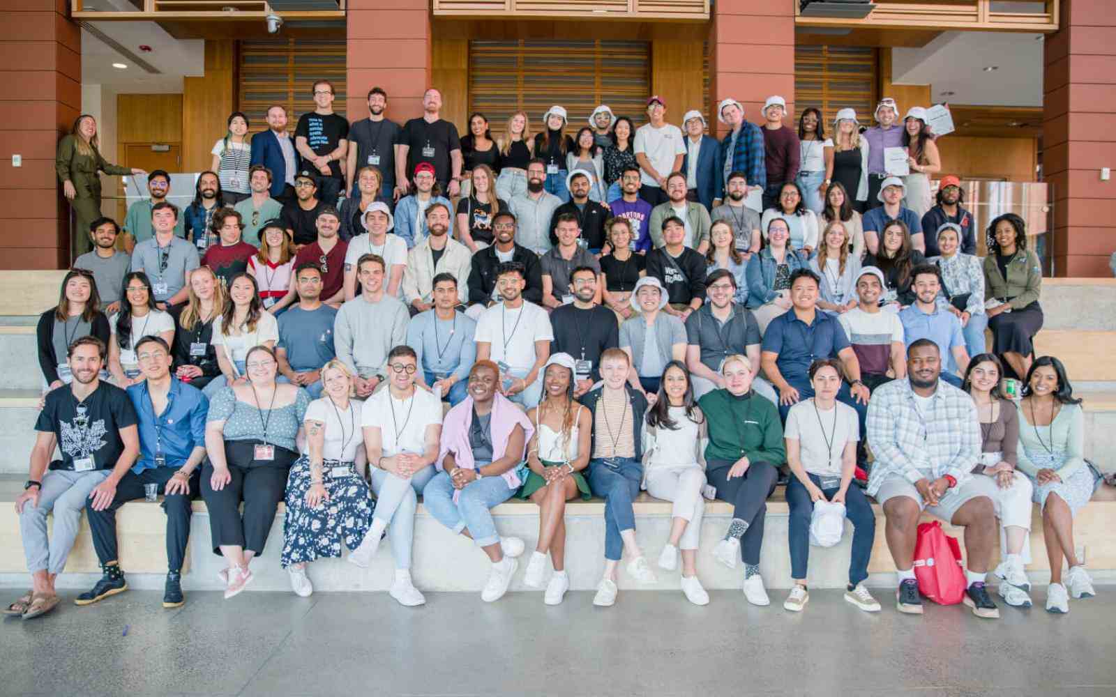 Group of about 100-150 young people seated on bleacher style seats smiling at the camera, as part of a Venture for Canada event