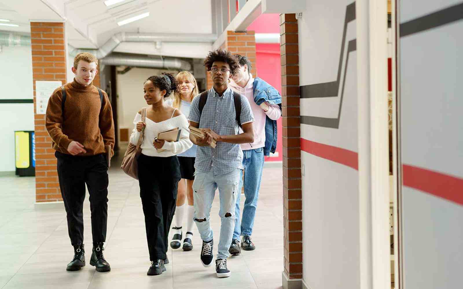 Four young adult aged students walking through a school hallway
