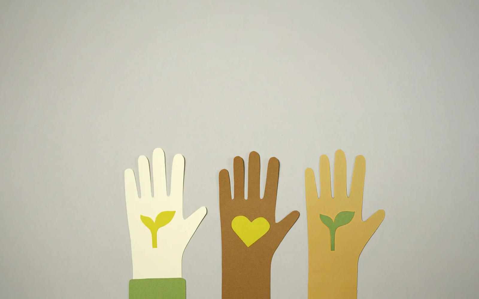 Three paper hands of different skin colors with plants inside the palm of the outside two and a heart inside the center one