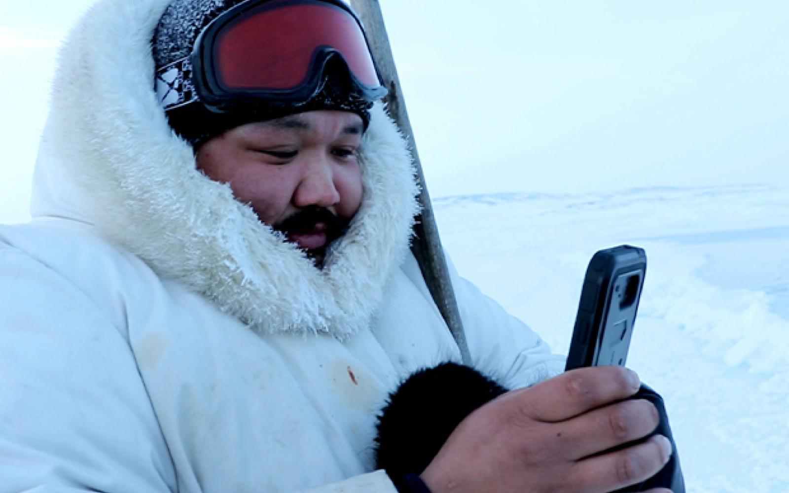 Person with white parka and ski goggles on using an app on a phone; background is a white snowy tundra