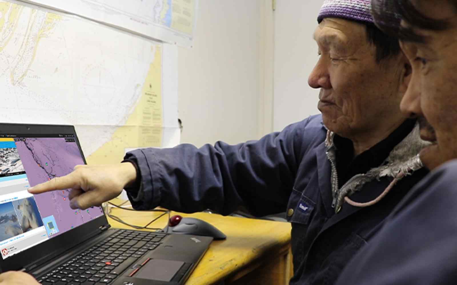 Two inuit elders gesturing at a laptop computer