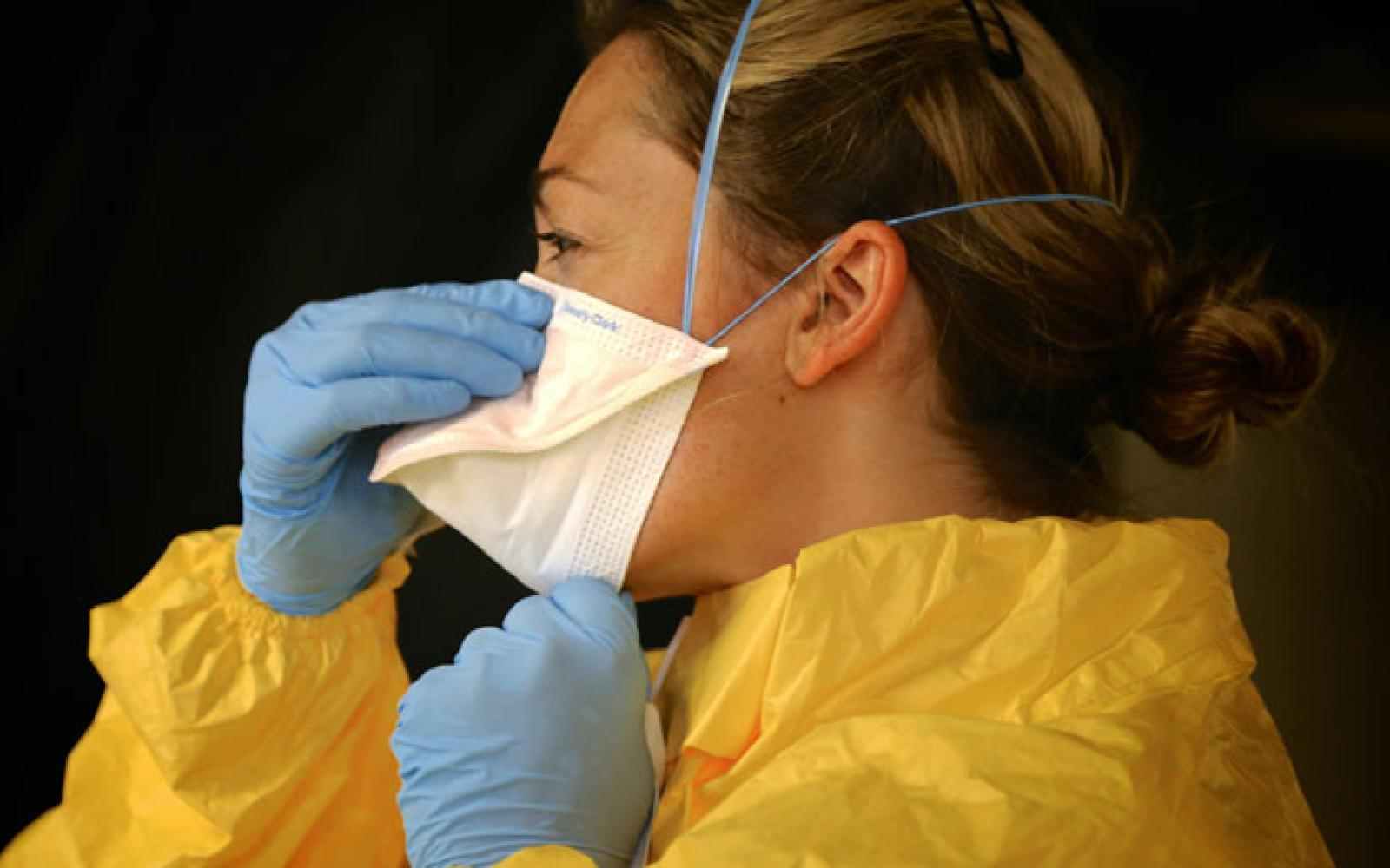 Person with protective body suit and gloves and facemask adjusting their facemask