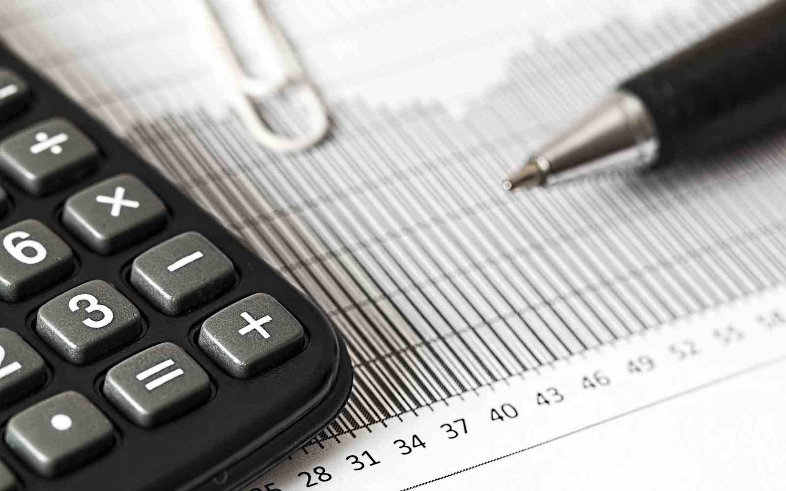 close up image of a graph, a pen, paper clip and caclulator on a white desk
