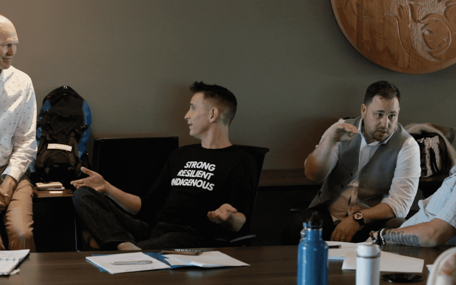 Four people discussing with each other in 1:1 pairs on two couches that are perpendicular to each other, in an indoor room with dark green wallpaper