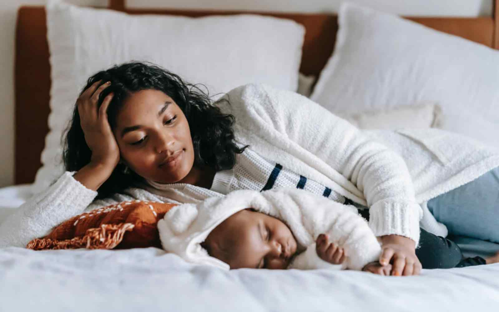 Photo of a Black mother with her child laying down on a bed with white sheets
