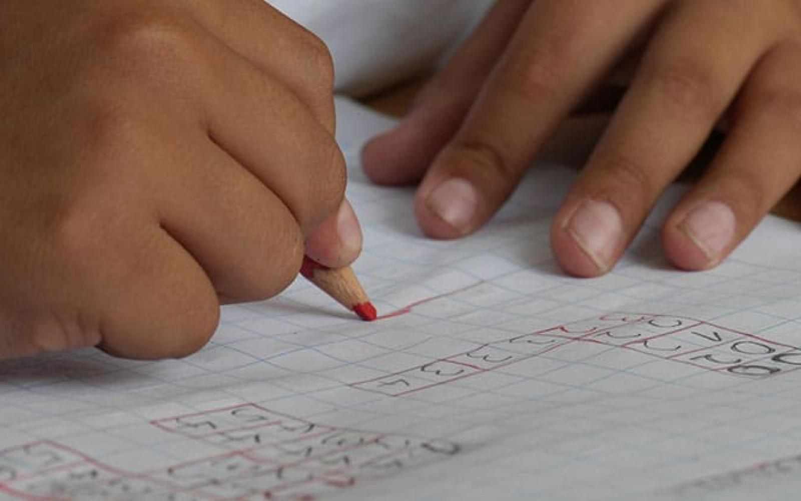 Close up of a youth's hands doing work on a piece of graph paper