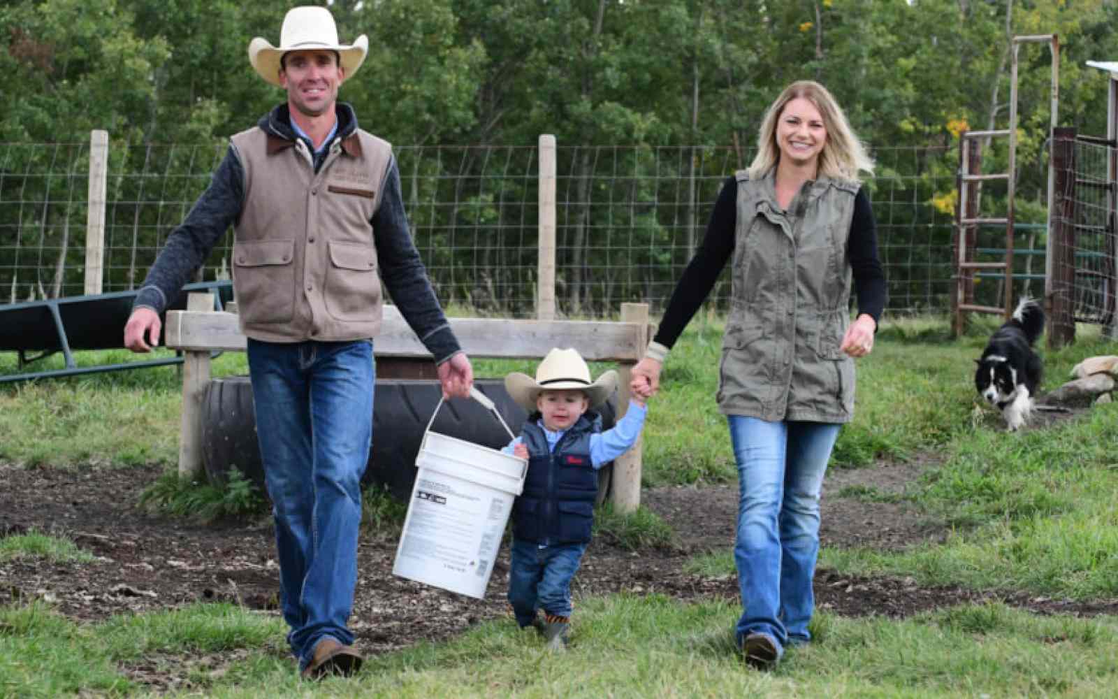 Photo of two farmers with their child carrying a bucket on their farmland