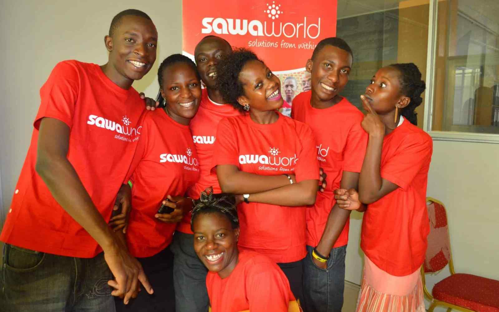 Group of youth from Uganda wearing red Sawa World t shirts smiling at the camera