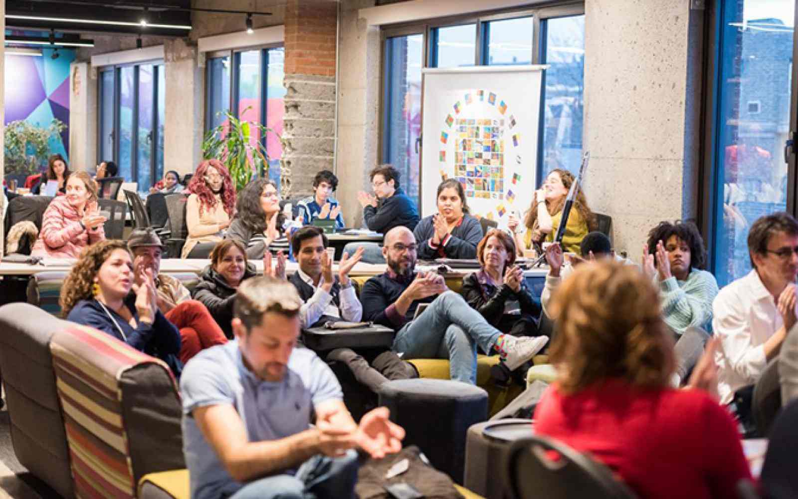 People seated in small groups in a large group at Dynamo's Hackathon