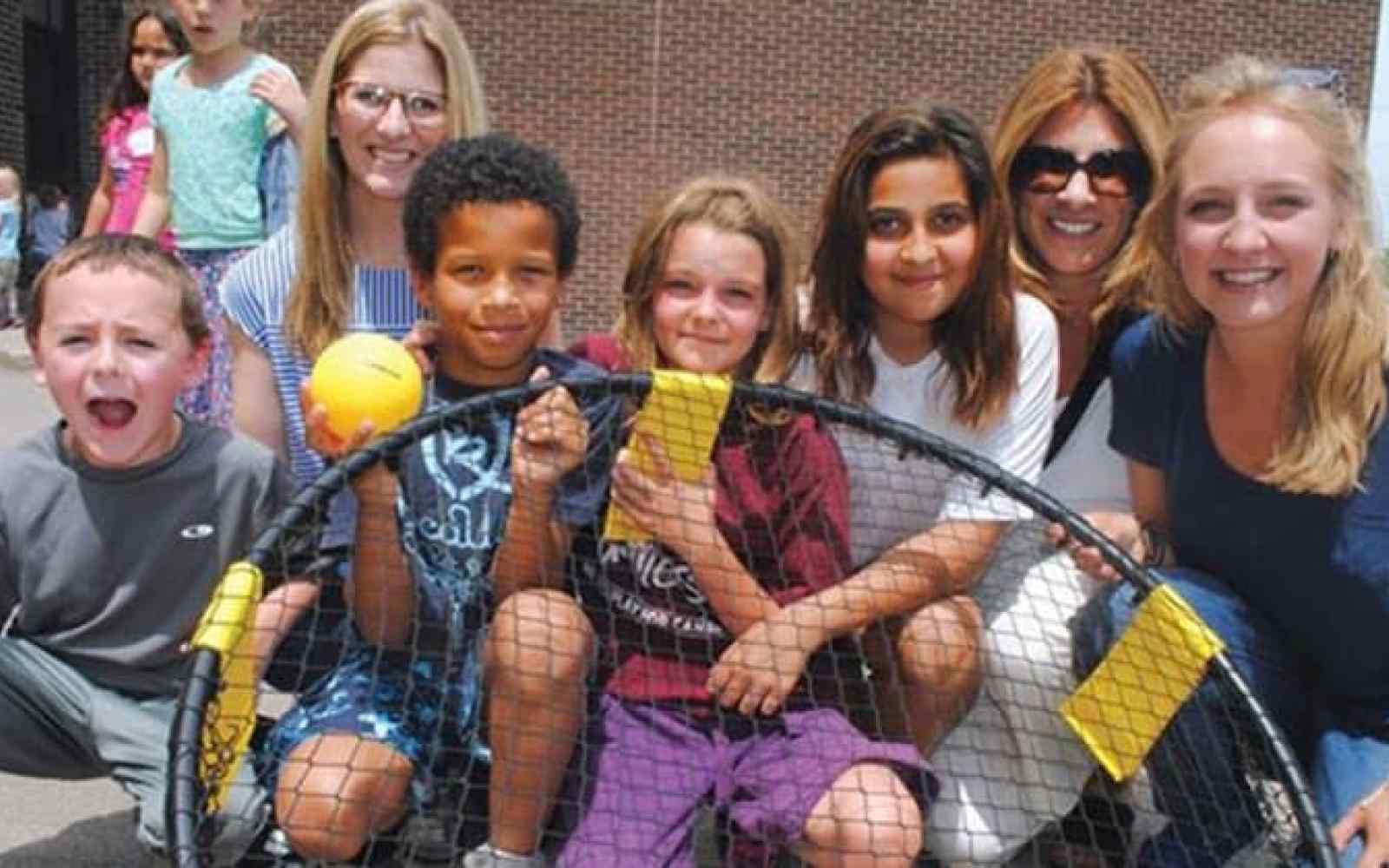 Photo of adults and elementary school aged kids playing spikeball at recess