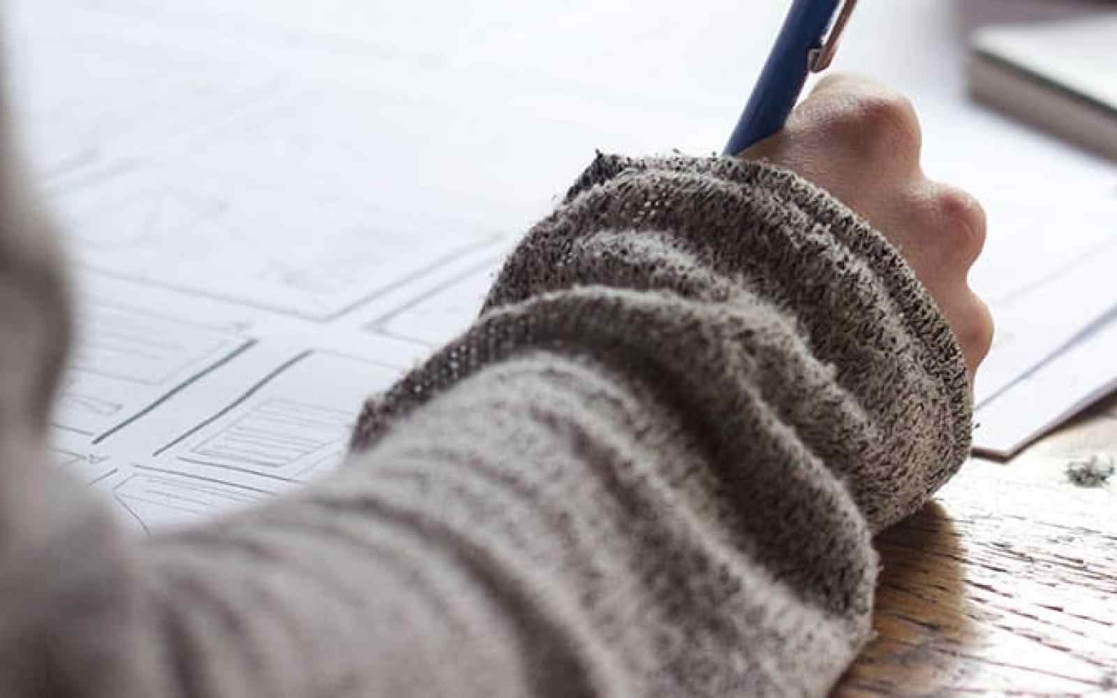 Photo of student's hand writing in a notebook on a desk