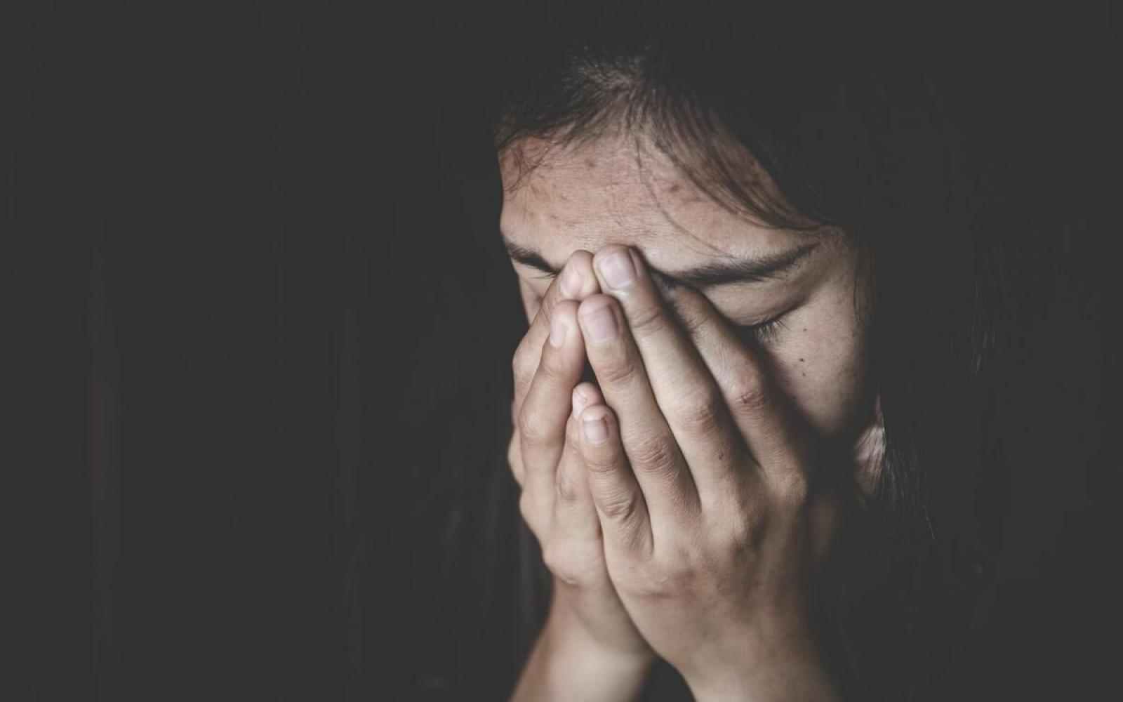 Woman with closed eyes and hands over her face; dark background