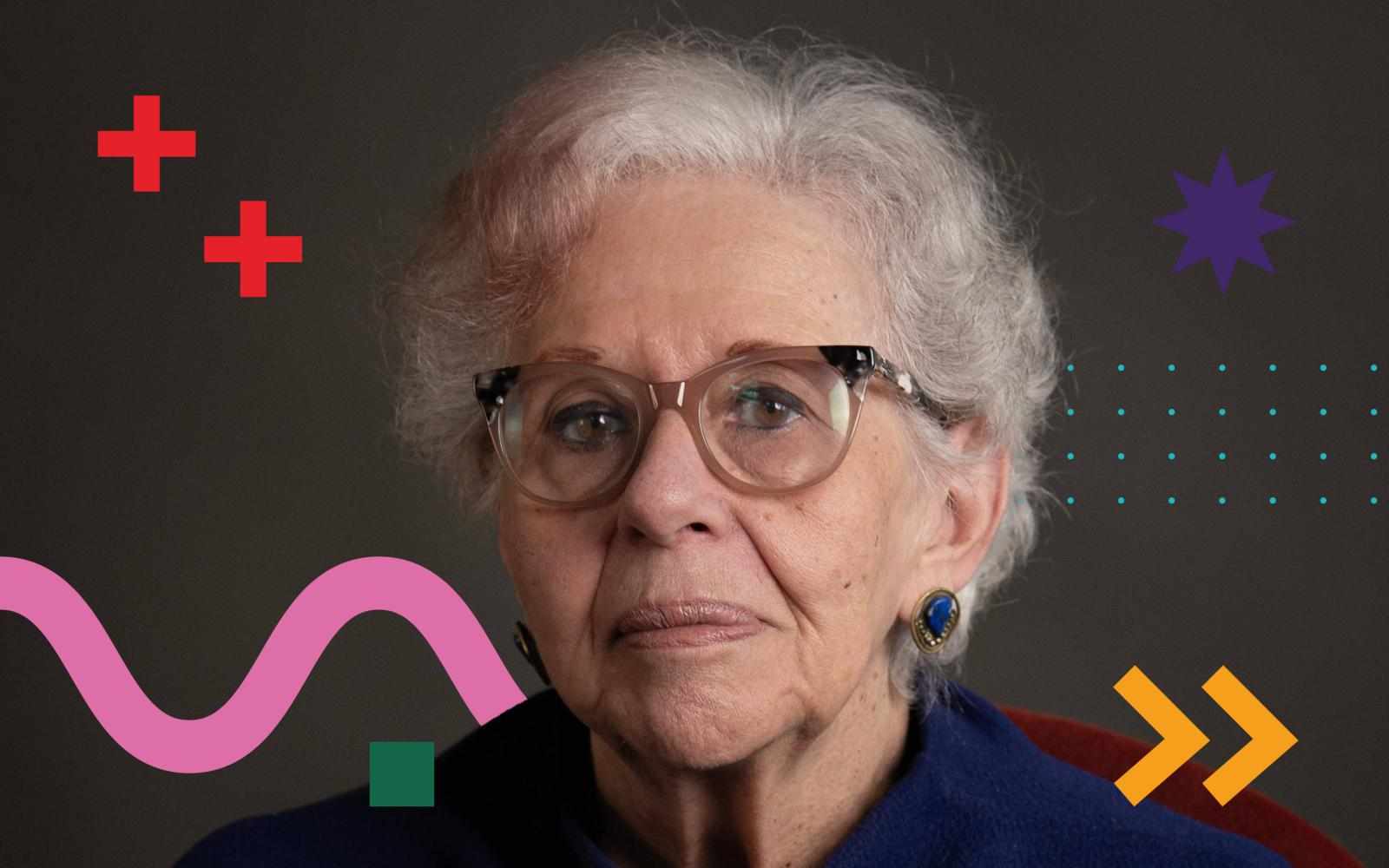 Portrait of Marta Gil, a person with short gray hair and round glasses, wearing blue clothing and a blue-stone earring, against a dark background with colorful graphic shapes (red crosses, purple star, dotted pattern, pink wave, and yellow arrows).