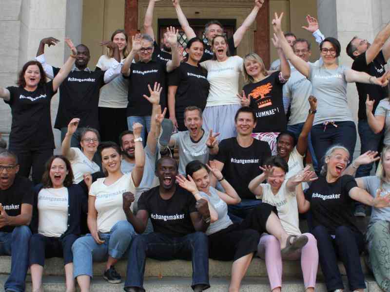 A group picture featuring diverse social innovators. They are smiling with their arms raised playfully. 