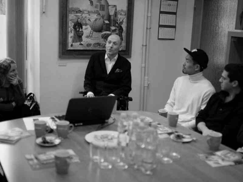 Czarno-białe zdjęcie Piotra Pawłowskiego - mówi do osób siedzących przy dużym stole.