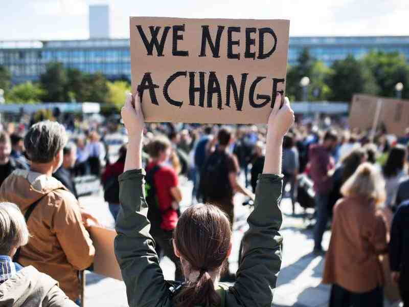 Young person at a rally of climate activist holding a sign that says "We need a change"