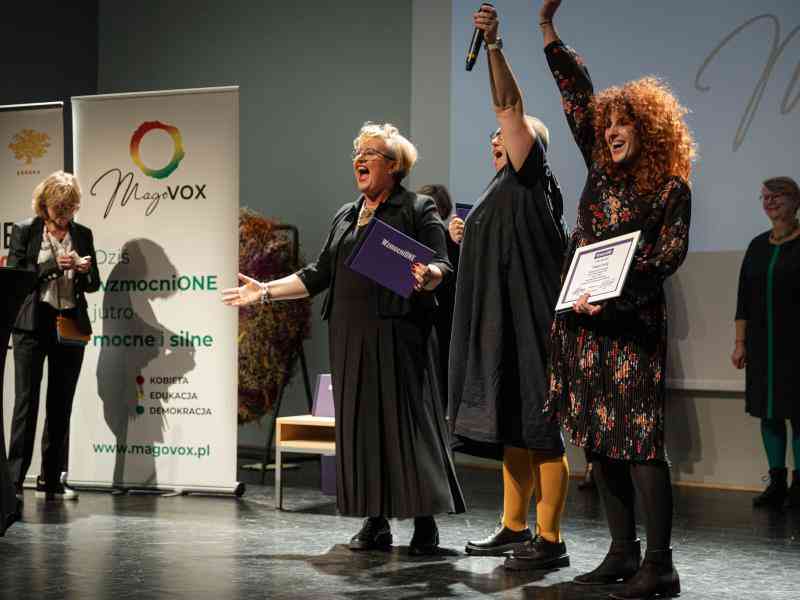 Zdjęcie przedstawia 3 członkinie Fundacji Oficyna-ToTutaj na scenie. Dwie podnoszą ręce w geście zwycięstwa, trzecia śmieje się z rozłożonymi rękami. W tle widać baner Ashoki i Magovoxu oraz uśmiechające się osoby z Jury programu.