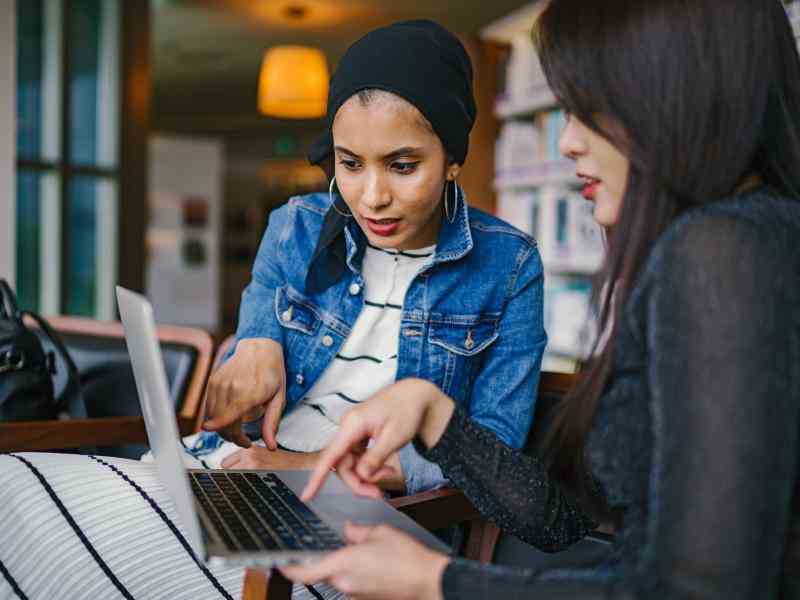 Two women sitting next do each other pointing at a computer screen