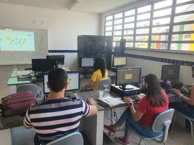 There are people in a classroom. They are using computers and there is an image of post-its on a board being projected in the front of the classroom.