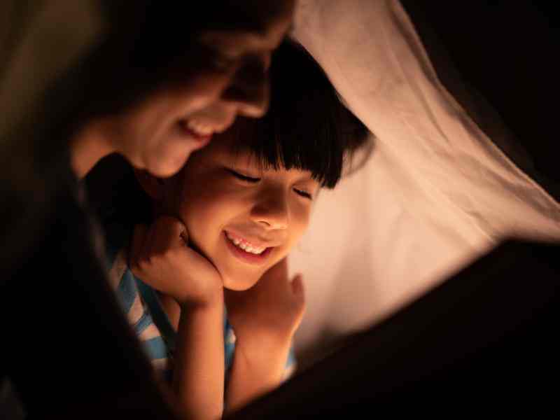 young Asian mother read the story in the book for her daughter children on the bed at home, family and motherhood learning concept