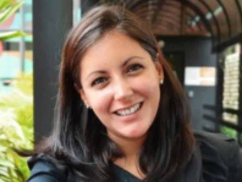 Photo of Lorena Garcia Duran, Director of DEI initiatives at Ashoka. Person with lighter skin and dark brown shoulder length hair smiling at the camera. Background of a covered walkway