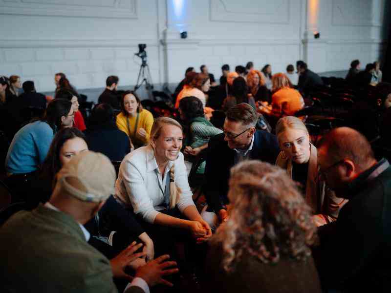 Photo of people sitting and conversing in small groups in a conference hall