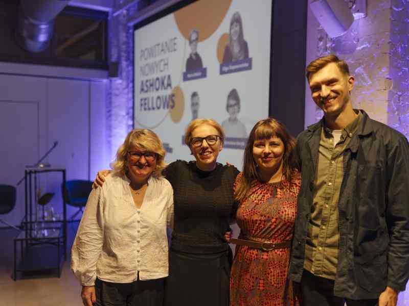 Zdjęcie przedstawia 4 Ashoka Fellows na spotkaniu witającym ich w społeczności Ashoki. Od lewej Myroslava Keryk, Maria Deskur, Olga Ślepowrońska i Maciej Otrębski. W tle widać filetowe światła i rzutnik.