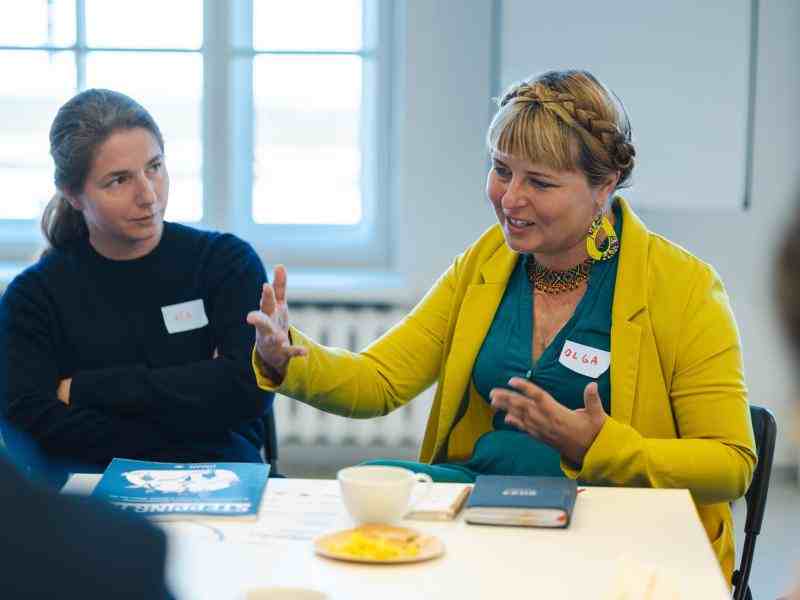 Two women sitting at the table, one is explaining somethig.