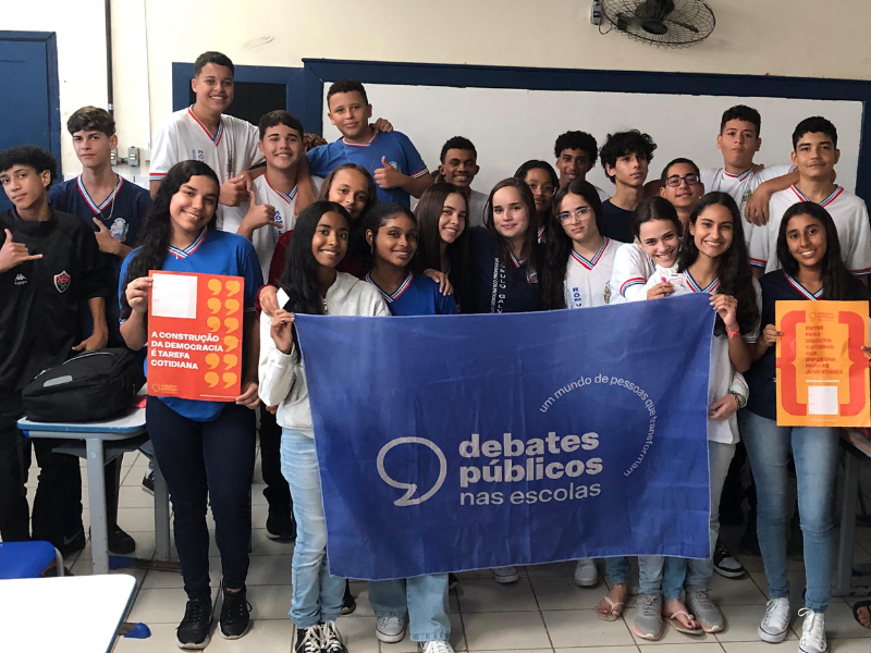 Um grupo de jovens reunidos segurando a bandeira dos Debates Públicos das Escolas