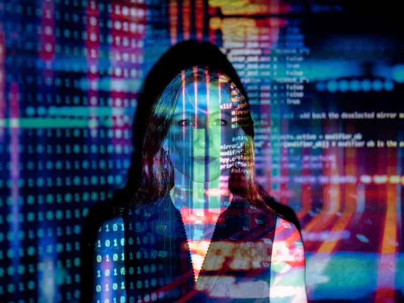 Mujer mirando a cámara en la que se reflejan códigos de programación 