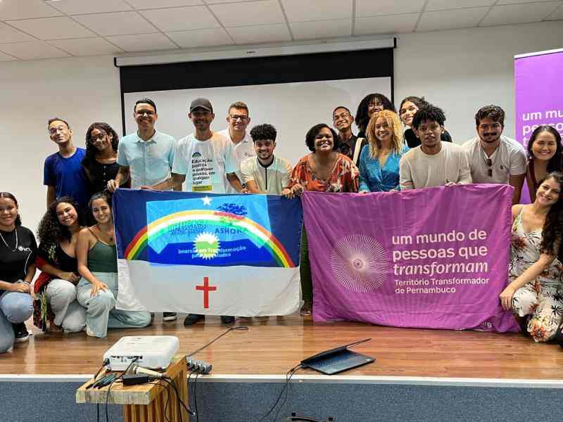 Diversas pessoas sorrindo em cima de um palco segurando as bandeiras do Pernambuco e do Território Transformador do Pernambuco