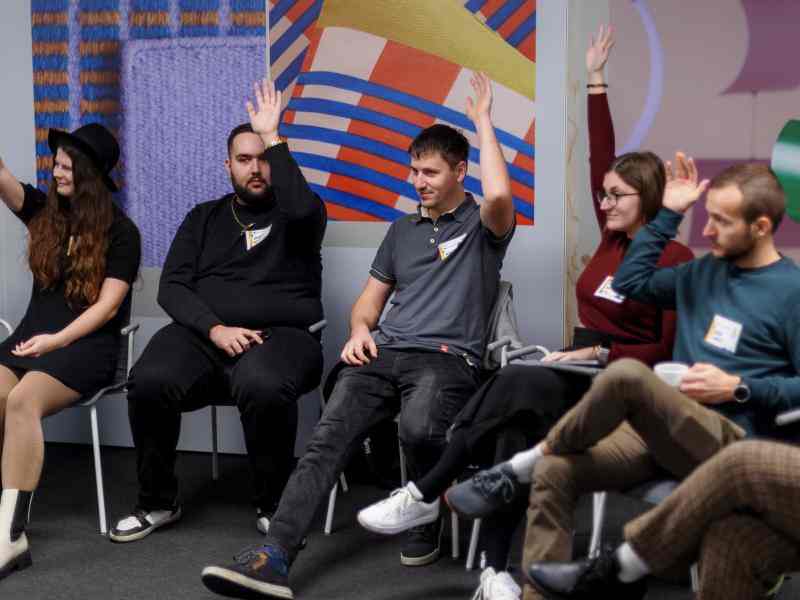 A group of young people sitting in a half circle, raising their hands