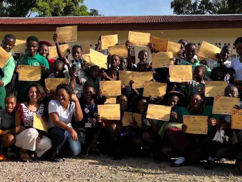 Group of young people and community members in Sierra Leone holding signs and smiling at the camera (backdrop of a building) as part of the SeeChange Initiative