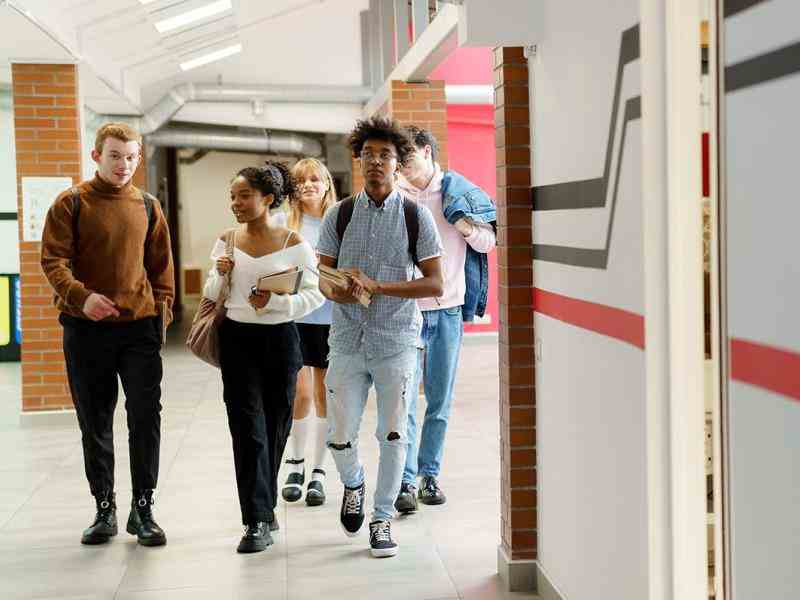 Four young adult aged students walking through a school hallway