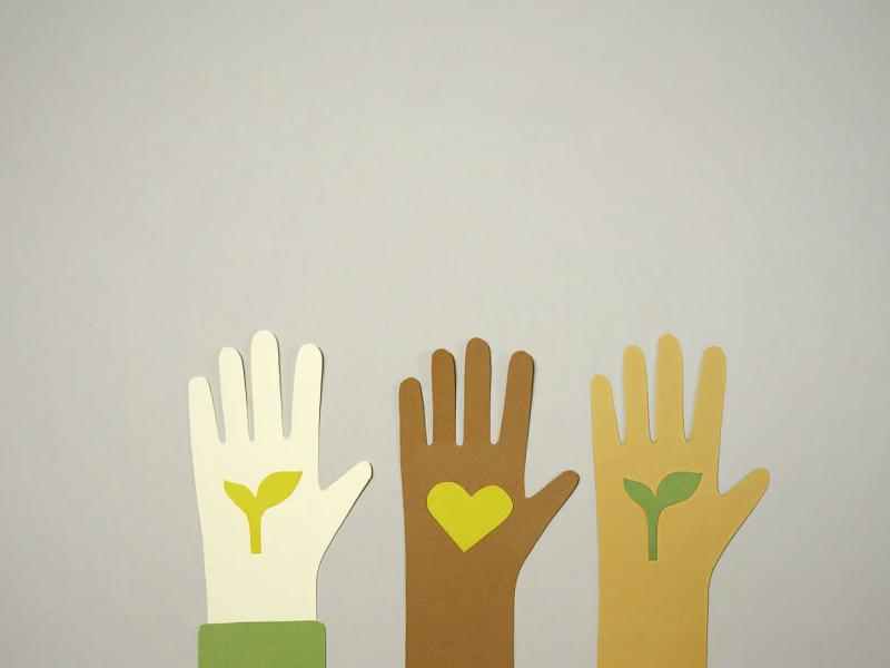 Three paper hands of different skin colors with plants inside the palm of the outside two and a heart inside the center one