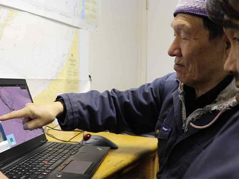 Two inuit elders gesturing at a laptop computer