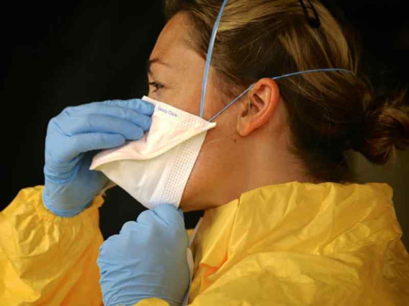 Person with protective body suit and gloves and facemask adjusting their facemask